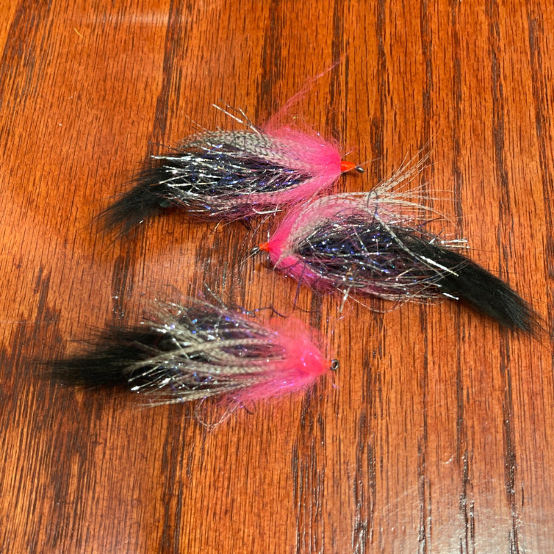 Three fishing lures with pink and black patterns on a wooden surface