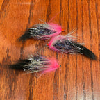 Three fishing lures with pink and black patterns on a wooden surface