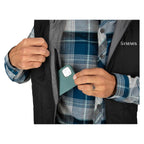 Person wearing a plaid shirt ywith a visible brand logo, holding a phone in a Simms MEN's Fall Run Insulated Vest w/CRO Logo pocket.