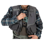 Person wearing a gray Simms Freestone Vest with a plaid shirt underneath, holding a phone.