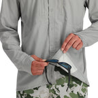Person wearing a light gray shirt and camouflage pants, holding sunglasses.
