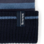 Navy and blue striped SIMMS Tip-Up Pom Beanie with a visible brand label on a white background