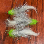 Three fly fishing flies with green bodies and white feathers on a wooden surface