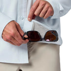 Person holding sunglasses with a Light blue Simms MEN's Men's Launch LS Shirt on a white background and beige pants