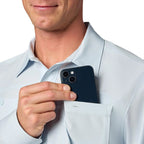 Man holding a smartphone in his Light blue Simms MEN's Men's Launch LS Shirt  pocket against a white background