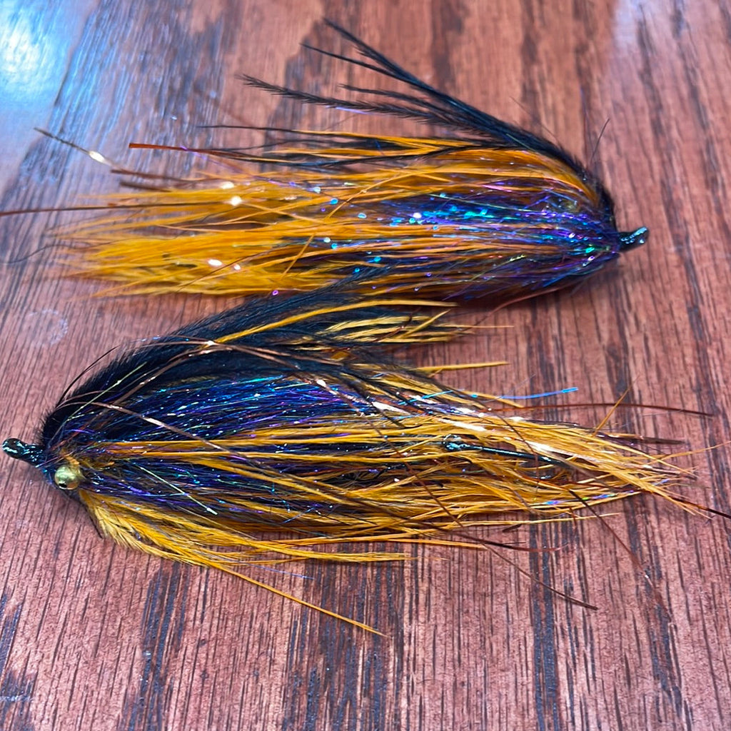 Fishing lure with orange and black feathers on a wooden surface