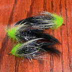 Two fishing flies with green and black patterns on a wooden surface