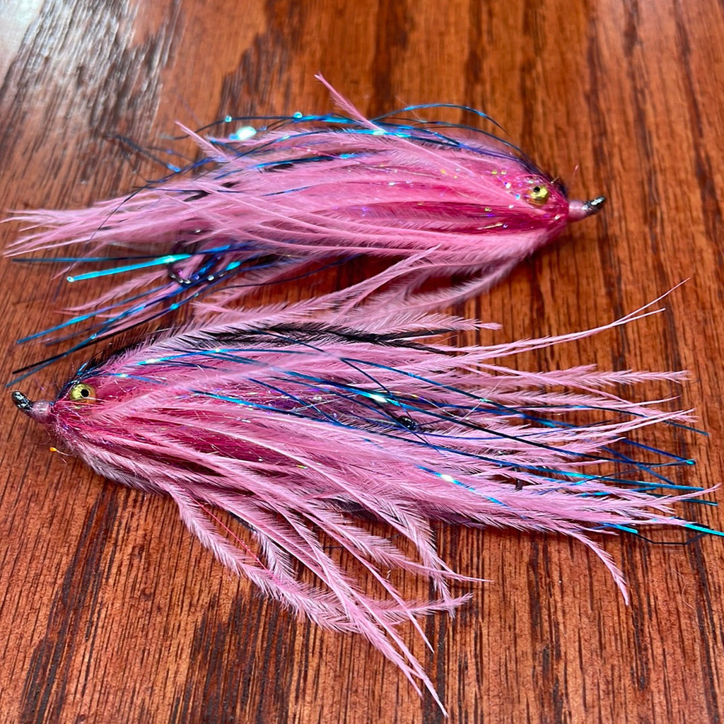 Two pink and black fishing lures on a wooden surface