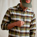 Person wearing a plaid Orvis MEN's Flat Creek Tech Flannel Shirt and cap with a logo, against a neutral background