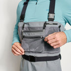 Close up of an angler wearing a pair of Orvis men's PRO LT fishing waders in gray color with adjustable elastic suspenders, neoprene booties, and a stretchy external pocket.