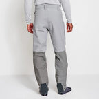 Angler wearing a pair of Orvis men's PRO LT wading pants in gray color with neoprene booties and a belt, designed for waist-high wading.