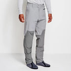 Angler wearing a pair of Orvis men's PRO LT wading pants in gray color with neoprene booties and a belt, designed for waist-high wading.