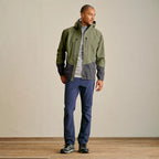 Man wearing a green and gray Orvis MEN's PRO Fishing Jacket with blue pants against a plain background