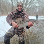 Man in camouflage clothing holding a fish in a snowy landscape
