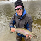 Person holding a fish in a body of water wearing winter clothing