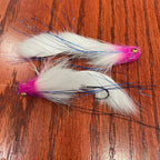 Two white and cerise artificial fishing flies designed for steelhead and salmon fishing, laid out on a wooden surface.