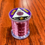 Spool of pink Wapsi Ultra Wire UTC with a label on a wooden surface