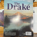 The cover of 'The Drake' magazine, featuring a scenic lake and mountain view, with the title and author's name at the top.