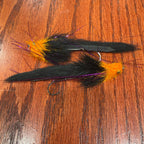 Two black and orange artificial fishing flies designed for steelhead and salmon fishing, laid out on a wooden surface.