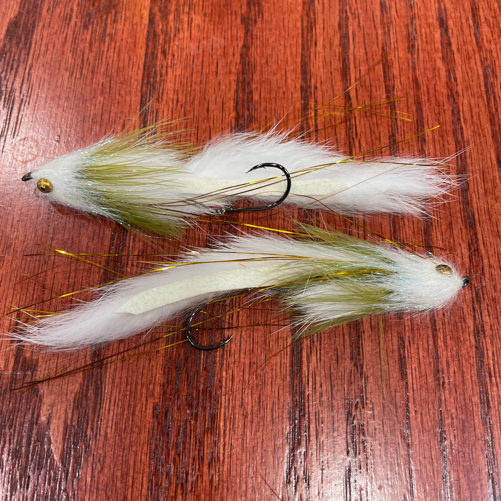 Two white and olive artificial fishing flies designed for steelhead and salmon fishing, laid out on a wooden surface.