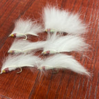 A set of six Lite Brite Zonker Fly fishing lures with white, yellow, and red colors on a wooden surface.