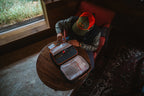 Person sitting at a table with a fly tying travel bag, surrounded by a cozy indoor setting.