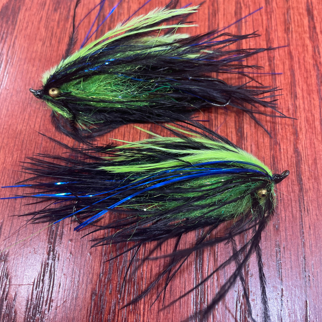 Two fishing lures with green and black feathers on a wooden surface