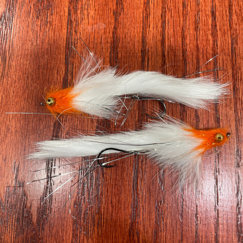 Two white and orange artificial fishing flies designed for steelhead and salmon fishing, laid out on a wooden surface.