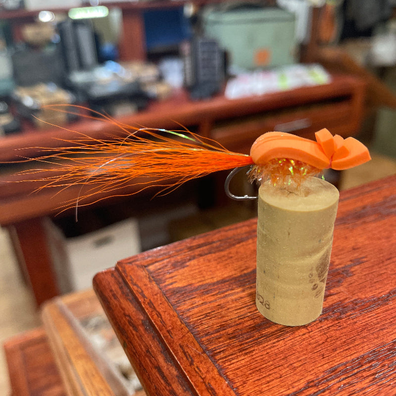 Fishing lure with orange feather on a wooden surface