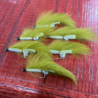 A collection of artificial fishing flies with white, black, and olive colors distributed across the frame, displayed on a wooden surface.