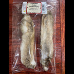A pair of Wapsi Hares Feet packaged in a clear plastic bag with a red and white product label that reads 'Chagrin River Outfitters - NATURAL WHITE.'.