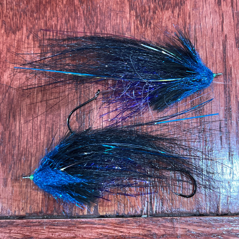 Two fishing lures with blue and black feathers on a wooden surface