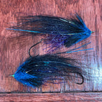 Two fishing lures with blue and black feathers on a wooden surface