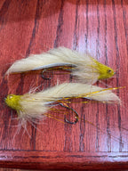 Two white and gold artificial fishing flies designed for steelhead and salmon fishing, laid out on a wooden surface.