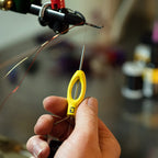 Hand holding a yellow Loon Ergo All Purpose Bobbin in the background