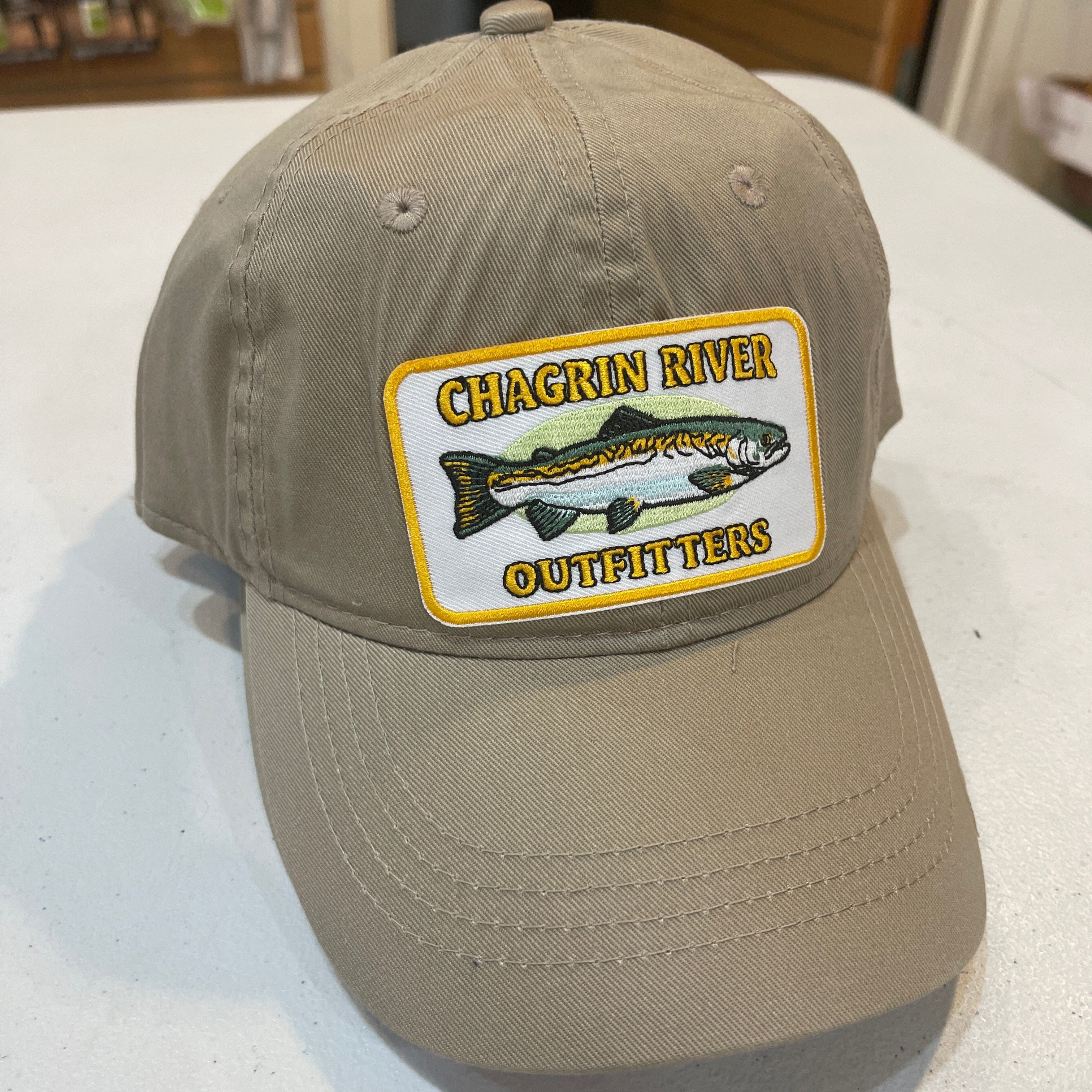 Beige cap with a fishing-themed patch on a white surface