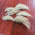A set of six Lite Brite Zonker Fly fishing lures with white, yellow, and red colors on a wooden surface.