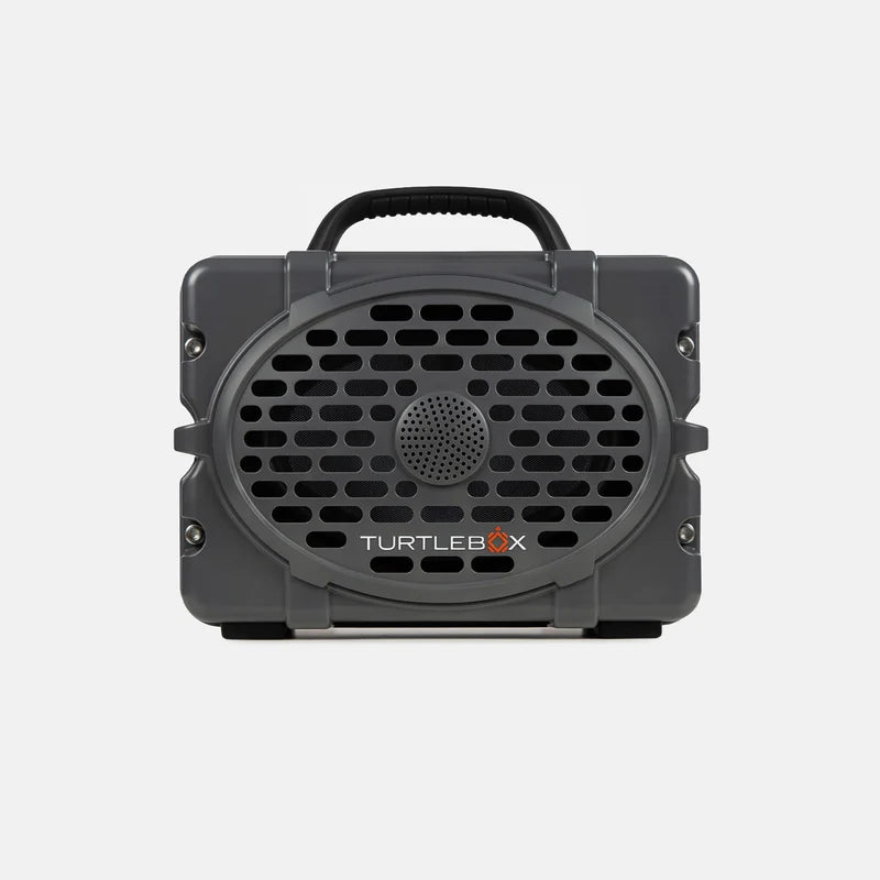 A dark gray portable speaker with a black handle and a front grille, featuring the TURTLEBOX logo in white and orange on a light gray background.