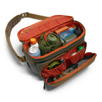 Open Simms Headwaters Sling Pack with various items including bottles and a green bag on a white background