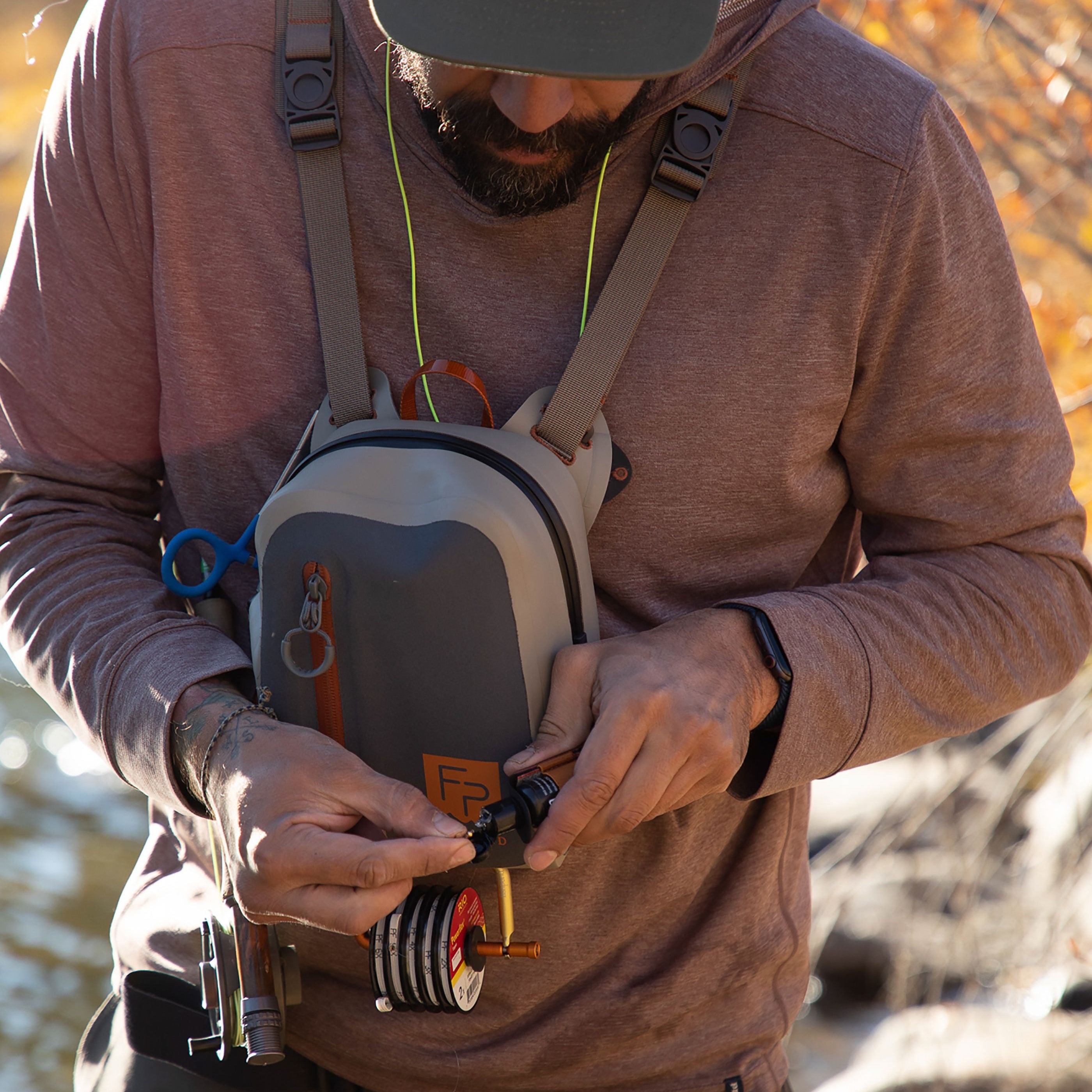 Person outdoors with a Fishpond Thunderhead® Submersible Chest Pack, holding equipment near water and trees.