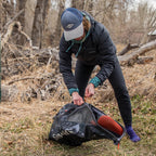 Person in outdoor setting with a Simms Taco Wader Bag w/CRO Logo, possibly in a forest or wooded area.