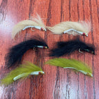 A set of six Lite Brite Zonker Fly fishing lures with green, yellow, and red colors on a wooden surface.