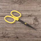 A pair of yellow-handled scissors with black blades placed on a wooden surface.