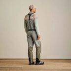 A man wearing Orvis breathable fly-fishing waders in gray and green colors, featuring external pockets and neoprene booties, standing against a plain background.
