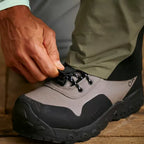 A man wearing Orvis breathable fly-fishing waders in gray and green colors with a pair of wading boots closeup. 