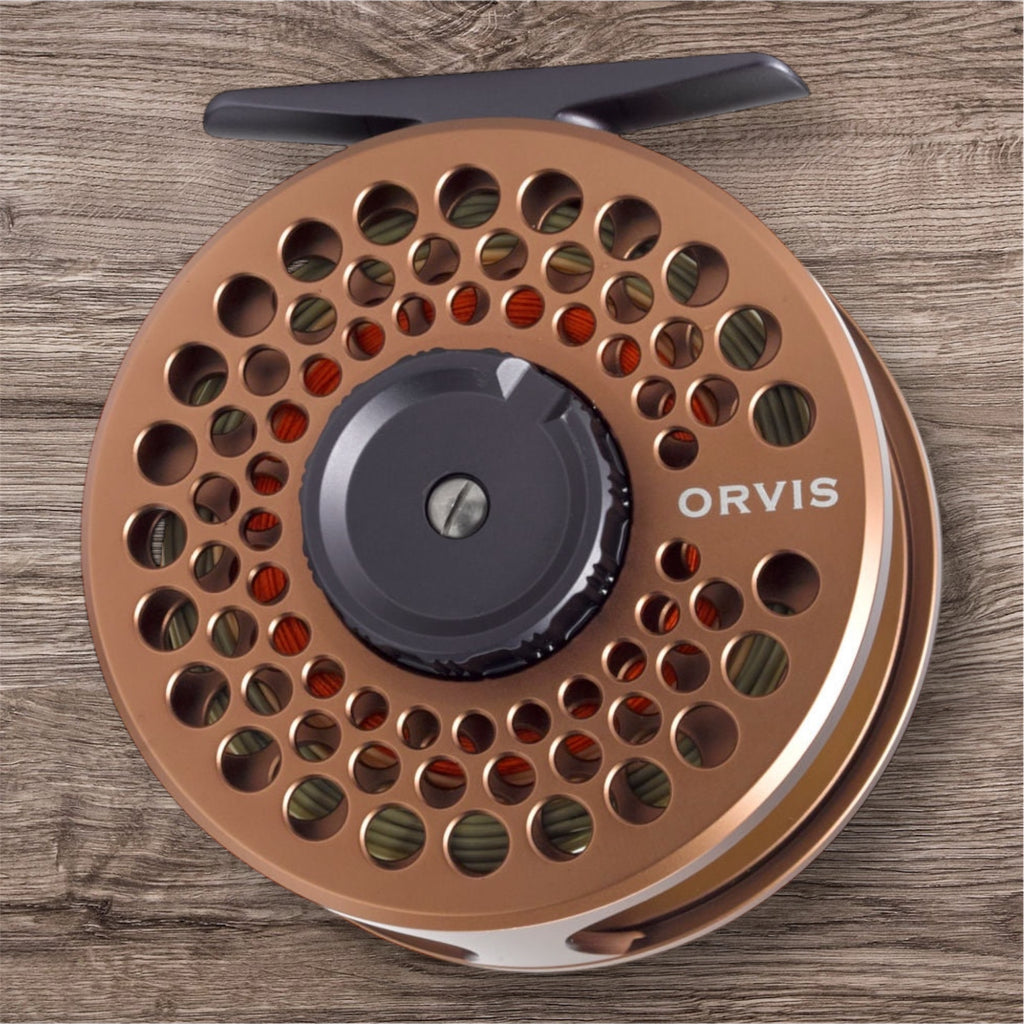 Orvis Battenkill Disc Fly Reel with a copper body and the brand name visible, placed on a wooden surface.
