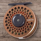 Orvis Battenkill Disc Fly Reel with a copper body and the brand name visible, placed on a wooden surface.