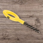 A Loon Ergo Dubbing Brush with a yellow powder-coated handle and black nylon bristles, placed on a wooden surface.