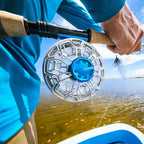 Fishing reel with Orvis logo held by a person on a boat, water and sky background