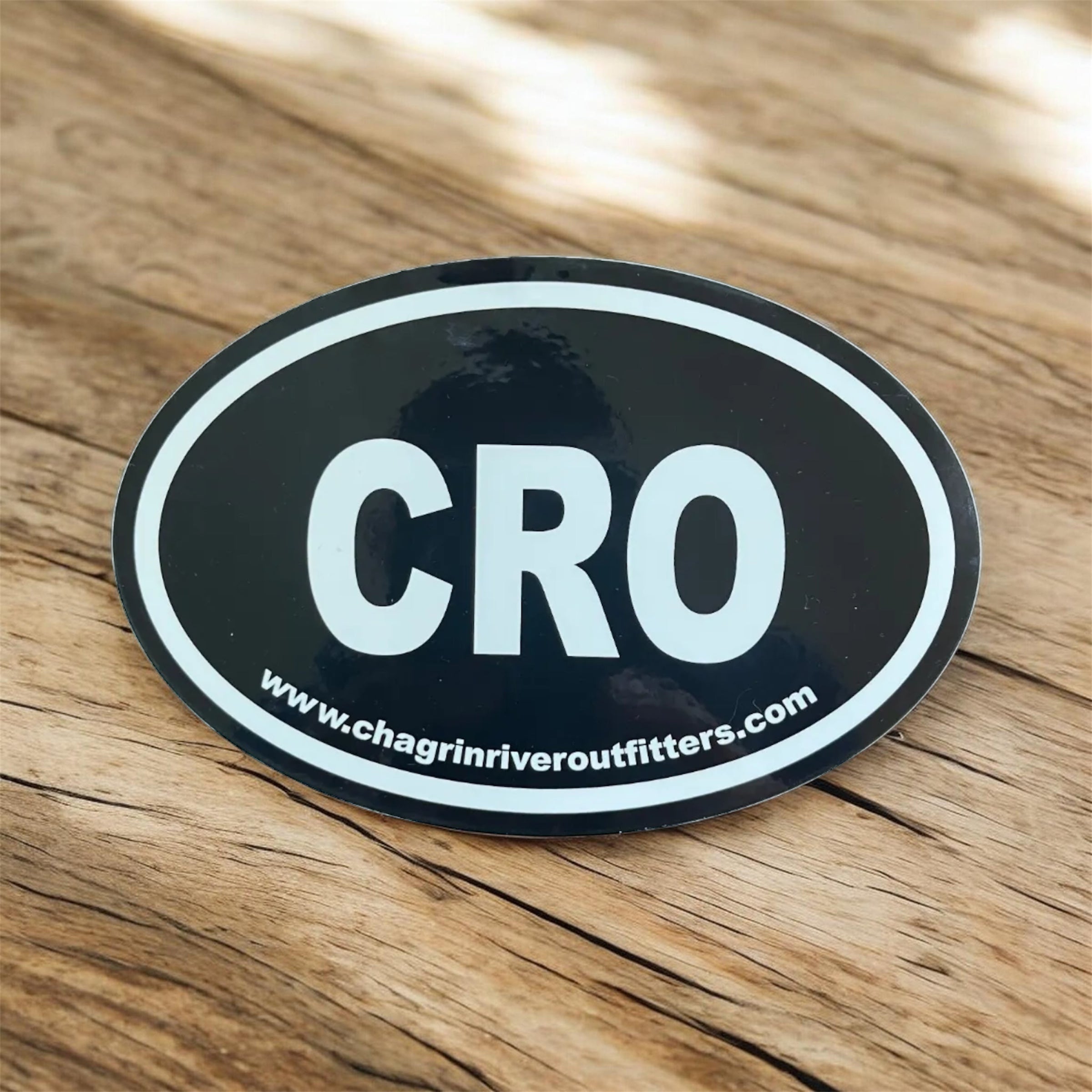 Black oval sticker with 'CRO' and website URL on a wooden surface